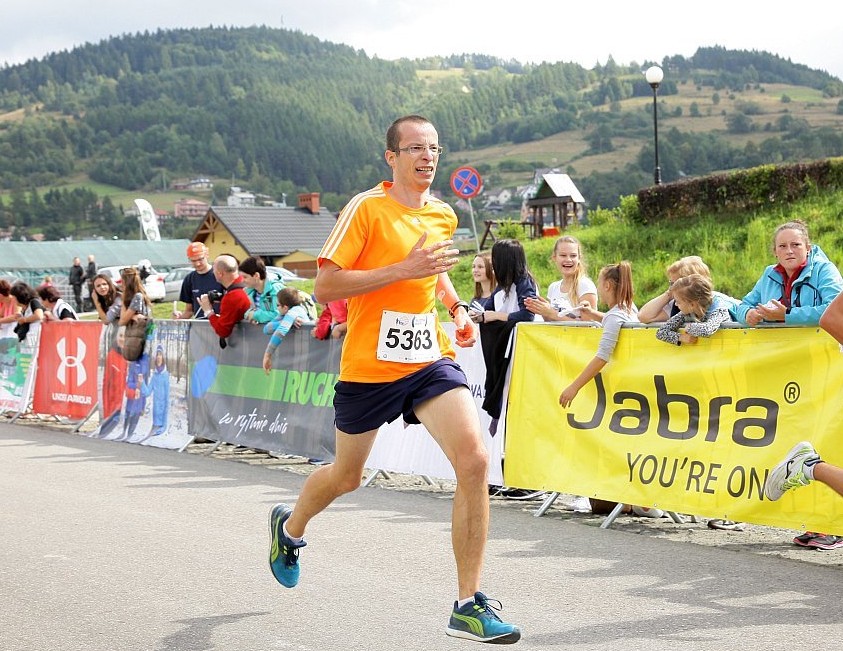 mężczyzna biegnie samotnie do mety na zawodach, w tle barierki, banery i kibice